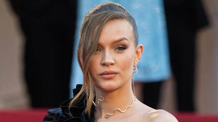 Josephine Skriver poses for the camera wearing a black one-shoulder dress and a gold choker necklace.